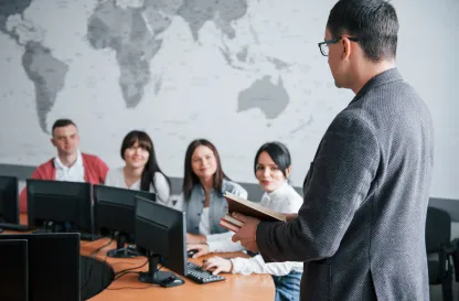 Podcasty | Uniwersytet Dolnośląski DSW we Wrocławiu: Wykładowca prowadzi zajęcia w sali komputerowej przed grupą studentów