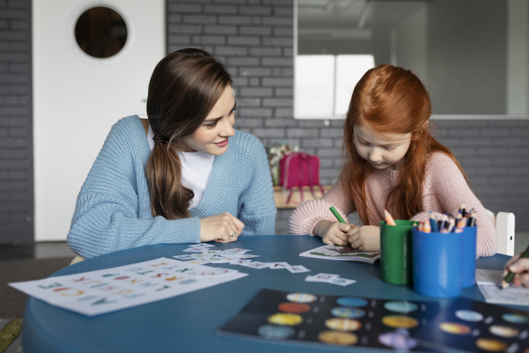 Język angielski w edukacji przedszkolnej i wczesnoszkolnej | Studia podyplomowe we Wrocławiu | Uniwersytet Dolnośląski DSW we Wrocławiu: Dziecko rysuje przy stole w towarzystwie dorosłej kobiety