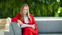 Akademia kompetencji lidera nowoczesnych technologii | Uniwersytet Dolnośląski DSW we Wrocławiu: studentka w czerwonym garniturze, siedzi na kanapie z notatkami