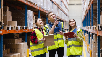 Logistyka przedsiębiorstwa z elementami ESG | Studia I stopnia we Wrocławiu | Uniwersytet Dolnośląski DSW we Wrocławiu: Studenci logistyki w neonowych kamizelkach spoglądają wspólnie na półki z kartonami