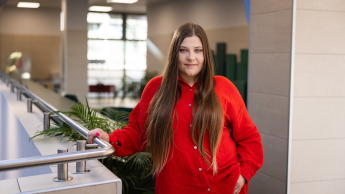 Logopedia | Studia podyplomowe we Wrocławiu | Uniwersytet Dolnośląski DSW we Wrocławiu: studentka w czerwonej koszuli oraz długich brązowych włosach, stoi na korytarzu