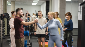 Zarządzanie organizacją sportową | Studia I stopnia we Wrocławiu | Uniwersytet Dolnośląski DSW we Wrocławiu: studenci na siłowni podający sobie ręcę