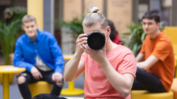 Personal branding z elementami AI | Uniwersytet Dolnośląski DSW we Wrocławiu: student w różowej koszulce robiący zdjęcie lustrzanką