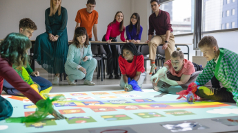  Grupa studentów i wykładowców podczas interaktywnej zabawy edukacyjnej z wykorzystaniem kolorowej projekcji na podłodze.