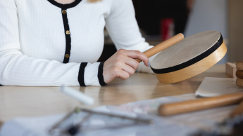 Wyniki wyszukiwania | Uniwersytet Dolnośląski DSW we Wrocławiu: Zbliżenie na ręce osoby trzymającej drewniany bębenek i pałeczkę podczas zajęć muzycznych.