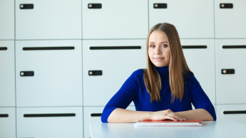 Bankowość cyfrowa | Uniwersytet Dolnośląski DSW we Wrocławiu: studentka w granatowym swetrze siedząca przy biurku na tle szafek 