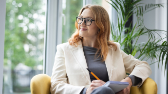 Edukacja i rehabilitacja osób z niepełnosprawnością intelektualną | Studia podyplomowe we Wrocławiu | Uniwersytet Dolnośląski DSW we Wrocławiu: Studentka siedzi na fotelu i przygotowuje notatki