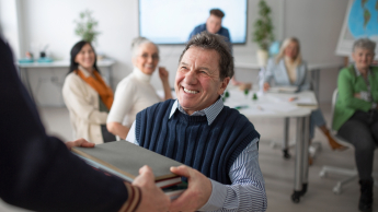 Dolnośląski Uniwersytet Trzeciego Wieku we Wrocławiu | Uniwersytet Dolnośląski DSW we Wrocławiu: Senior siedzący na krześle, trzymający laptopa.