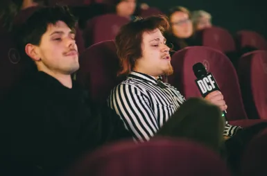 Studencki Dyskusyjny Klub Filmowy UDDSW zaprasza na kolejny film | 03.03.2026 | Aktualności | Uniwersytet Dolnośląski DSW we Wrocławiu: mężczyzna odpowiadający na pytania w sali kinowej