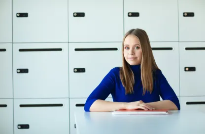 Aktualności | Uniwersytet Dolnośląski DSW we Wrocławiu: studentka w granatowym swetrze siedząca przy biurku na tle szafek 