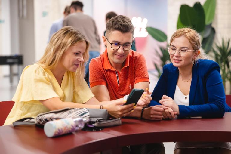 Dział Współpracy Międzynarodowej i Welcome Center | Uniwersytet Dolnośląski DSW we Wrocławiu: Główna grafika: Dział Współpracy z Zagranicą - studenci wspólnie oglądający treści na telefonie