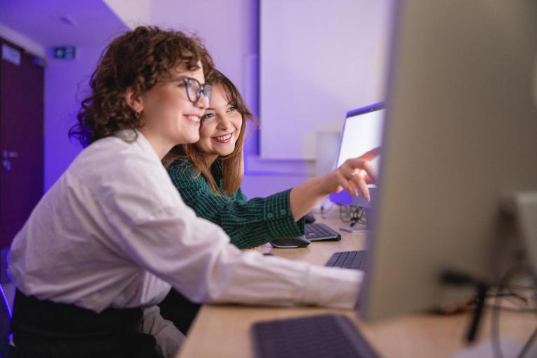 Programista gier komputerowych | Studia I stopnia we Wrocławiu | Uniwersytet Dolnośląski DSW we Wrocławiu: Grafika główna: Zniżki i dofinansowanie szkolenia i kursy - studentki oglądające materiał na komputerze