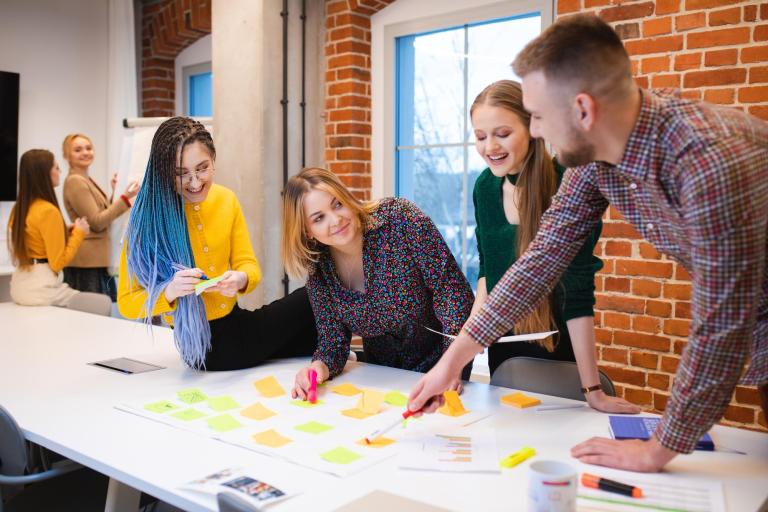 Media design i marketing wizerunkowy | Studia I stopnia we Wrocławiu | Uniwersytet Dolnośląski DSW we Wrocławiu: Grupa studentów rozpisująca projekt na biurku.