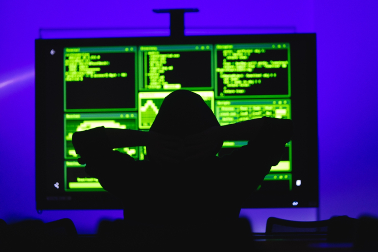 Zarządzanie cyberbezpieczeństwem | Studia I stopnia we Wrocławiu | Uniwersytet Dolnośląski DSW we Wrocławiu: czarna postać w kapturze siedząca na przeciwko ekranu z zaszyfrowanymi danymi
