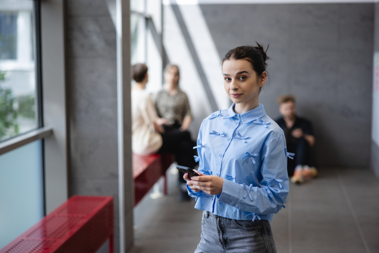 Technologie dźwiękowe w produkcji multimedialnej | Studia I stopnia we Wrocławiu | Uniwersytet Dolnośląski DSW we Wrocławiu: studentka w niebieskiej koszuli z telefonem w ręku