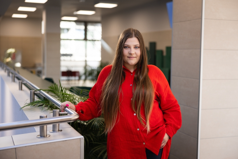 Energetyka wiatrowa (Onshore & Offshore) | Studia podyplomowe we Wrocławiu | Uniwersytet Dolnośląski DSW we Wrocławiu: studentka w czerwonej koszuli oraz długich brązowych włosach, stoi na korytarzu