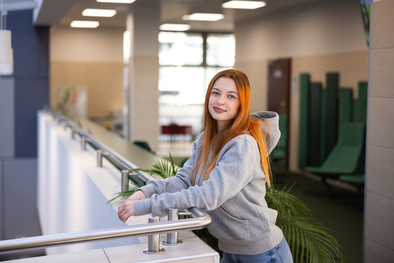 AI design i automatyzacja w marketingu | Studia I stopnia we Wrocławiu | Uniwersytet Dolnośląski DSW we Wrocławiu: studentka w szarej bluzie i rudych włosach, opierająca się o barierkę