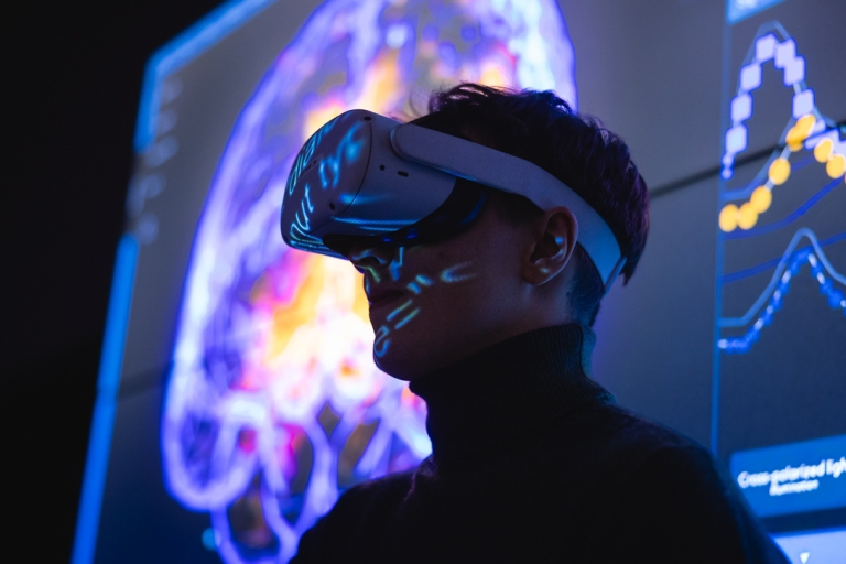 AI w psychologii i analityce behawioralnej | Studia I stopnia we Wrocławiu | Uniwersytet Dolnośląski DSW we Wrocławiu: Student w okularach VR, w tle widnieje wizualizacja ludzkiego mózgu