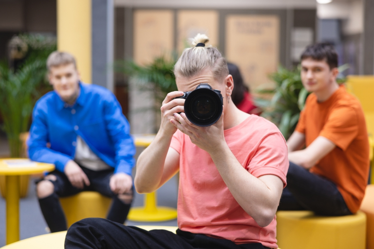Komunikacja wizerunkowa | Studia II stopnia we Wrocławiu | Uniwersytet Dolnośląski DSW we Wrocławiu: student w różowej koszulce robiący zdjęcie lustrzanką