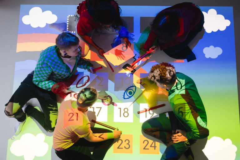 Pedagogika resocjalizacyjna | Studia I stopnia we Wrocławiu | Uniwersytet Dolnośląski DSW we Wrocławiu: Widok z góry na grupę osób pracujących na kolorowej, świetlnej podłodze z ilustracjami i liczbami.