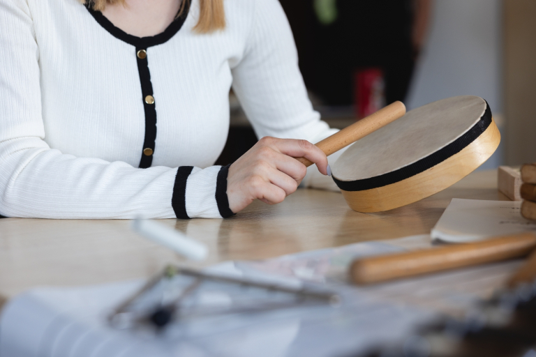 Pedagogika | Studia II stopnia we Wrocławiu | Uniwersytet Dolnośląski DSW we Wrocławiu: Zbliżenie na ręce osoby trzymającej drewniany bębenek i pałeczkę podczas zajęć muzycznych.