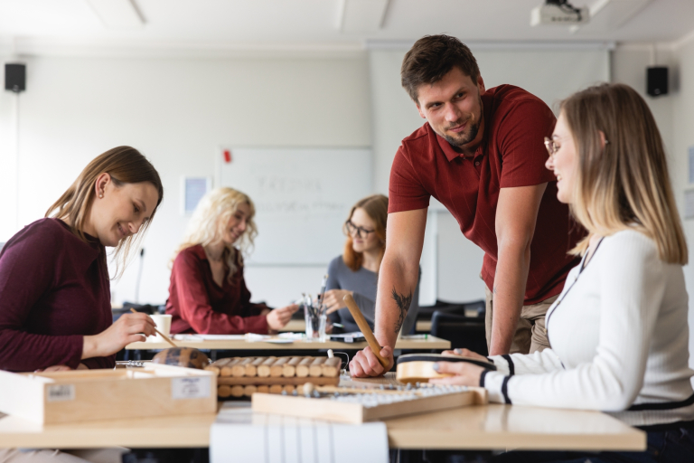 Pedagogika | Studia II stopnia we Wrocławiu | Uniwersytet Dolnośląski DSW we Wrocławiu: Studenci pracują przy stołach z instrumentami muzycznymi podczas zajęć praktycznych z pedagogiki.