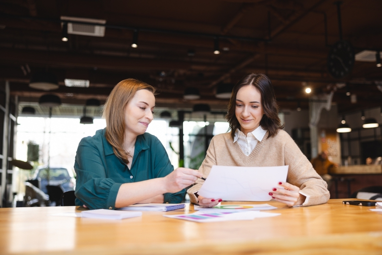 Copywriting - jako narzędzie sprzedaży i reklamy | Studia podyplomowe we Wrocławiu | Uniwersytet Dolnośląski DSW we Wrocławiu: dwie studentki wspólnie oglądające dane na kartce papieru