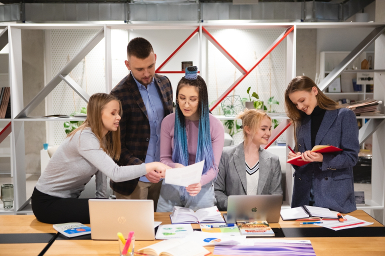 Zarządzanie | Studia II stopnia we Wrocławiu | Uniwersytet Dolnośląski DSW we Wrocławiu: grupa 5 studentów wspólnie pracująca nad projektem. Na stole leżą rozłożone notatki i laptopy.