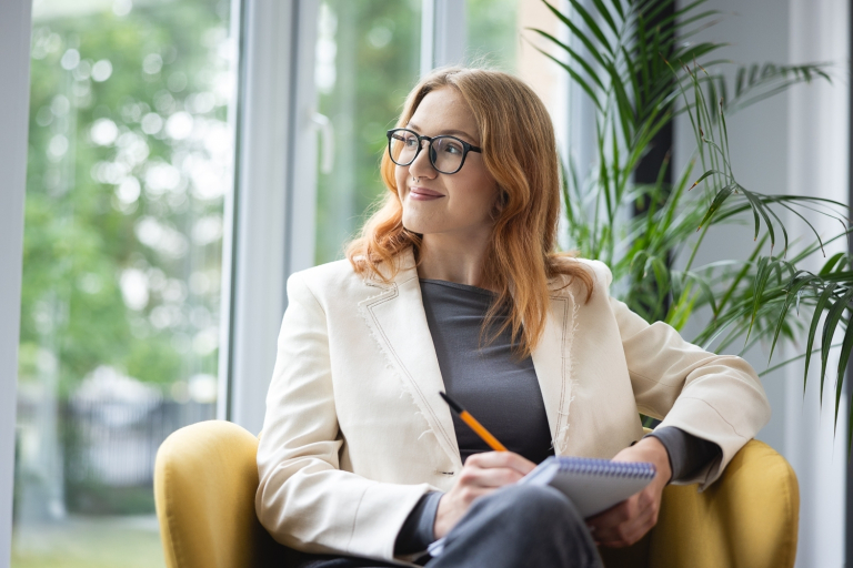 Podatki i doradztwo podatkowe | Studia podyplomowe we Wrocławiu | Uniwersytet Dolnośląski DSW we Wrocławiu: Studentka siedzi na fotelu i przygotowuje notatki