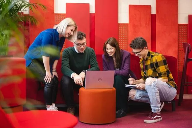 Poznaj nas | Uniwersytet Dolnośląski DSW we Wrocławiu: Trójka studentów wraz z wykładowcą, wspólnie robią notatki na komputerze oraz w notesie.