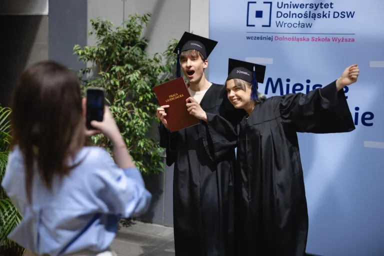 Wyniki wyszukiwania | Uniwersytet Dolnośląski DSW we Wrocławiu: Zdjęcie dwóch studentów w togach i pracą licencjacką.