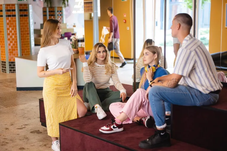 Buddy Program | Uniwersytet Dolnośląski DSW we Wrocławiu: Główna grafika: Dział Współpracy z Zagranicą - grupa studentów rozmawiająca na pufach