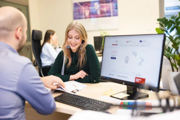 Zarządzanie | Studia I stopnia we Wrocławiu | Uniwersytet Dolnośląski DSW we Wrocławiu: „Mężczyzna i kobieta siedzą przy biurku w biurze, rozmawiają i przeglądają dokumenty; na pierwszym planie ekran komputera.”