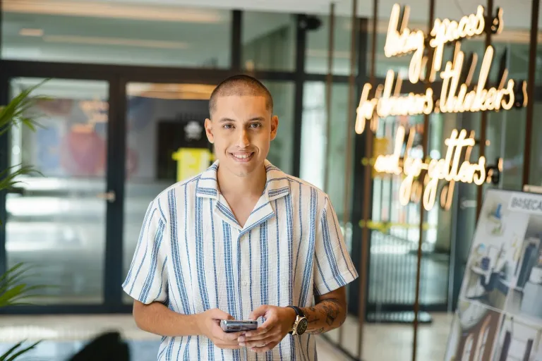 Zarządzanie sprzedażą i e-commerce | Studia I stopnia we Wrocławiu | Uniwersytet Dolnośląski DSW we Wrocławiu: Student w koszuli w paski trzymający telefon