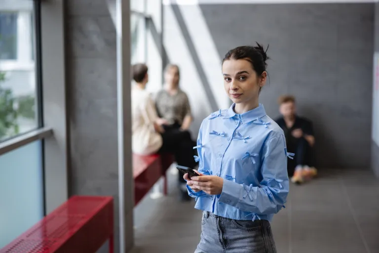 Nasz kampus | Uniwersytet Dolnośląski DSW we Wrocławiu: studentka w niebieskiej koszuli z telefonem w ręku