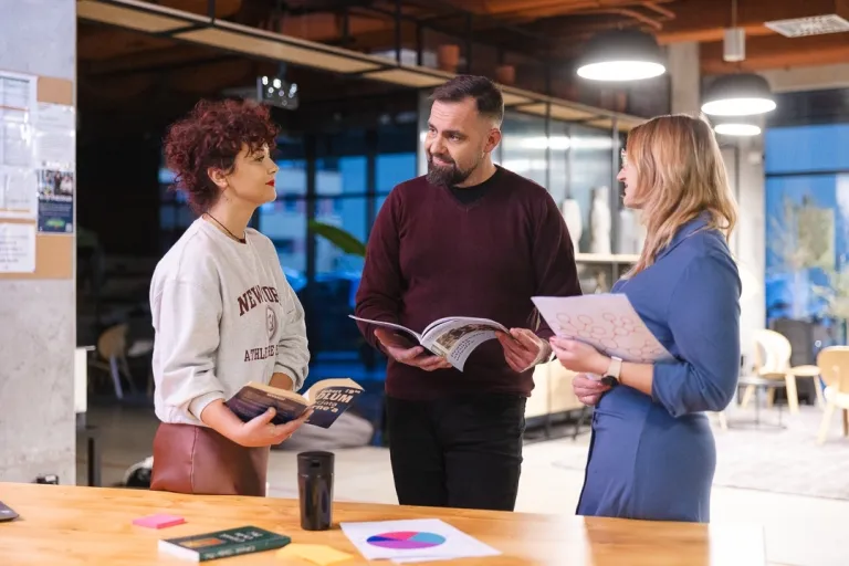 Weź udział w projekcie „Szkoła Dostępności Cyfrowej” (SDC) | Aktualności | Uniwersytet Dolnośląski DSW we Wrocławiu: trójka studentów stojąca przy biurko z notatkami