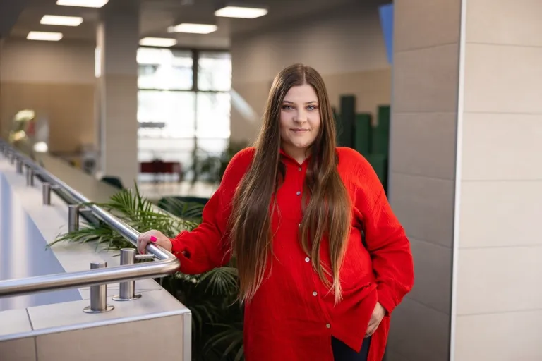 Komunikacja wizerunkowa | Studia II stopnia we Wrocławiu | Uniwersytet Dolnośląski DSW we Wrocławiu: studentka w czerwonej koszuli oraz długich brązowych włosach, stoi na korytarzu