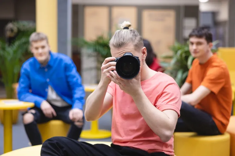 Produkcja audiowizualna | Studia I stopnia we Wrocławiu | Uniwersytet Dolnośląski DSW we Wrocławiu: student w różowej koszulce robiący zdjęcie lustrzanką