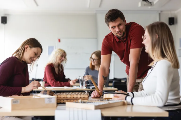 Pedagogika resocjalizacyjna | Studia I stopnia we Wrocławiu | Uniwersytet Dolnośląski DSW we Wrocławiu: Studenci pracują przy stołach z instrumentami muzycznymi podczas zajęć praktycznych z pedagogiki.