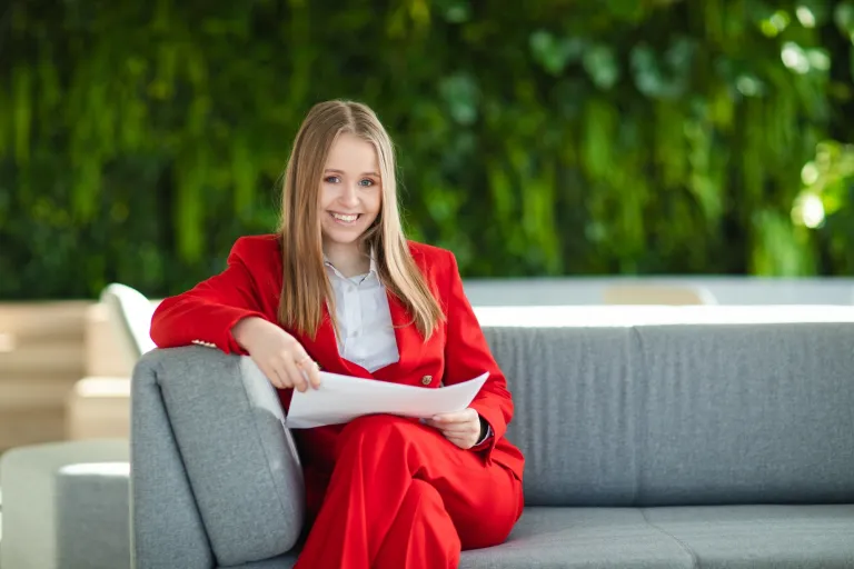 Zarządzanie | Studia II stopnia we Wrocławiu | Uniwersytet Dolnośląski DSW we Wrocławiu: studentka w czerwonym garniturze, siedzi na kanapie z notatkami