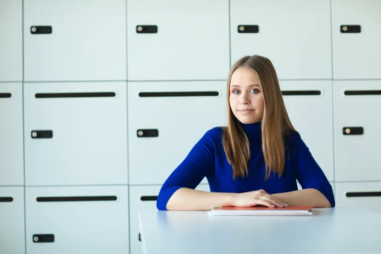 Administracja celno-skarbowa | Studia I stopnia we Wrocławiu | Uniwersytet Dolnośląski DSW we Wrocławiu: studentka w granatowym swetrze siedząca przy biurku na tle szafek 