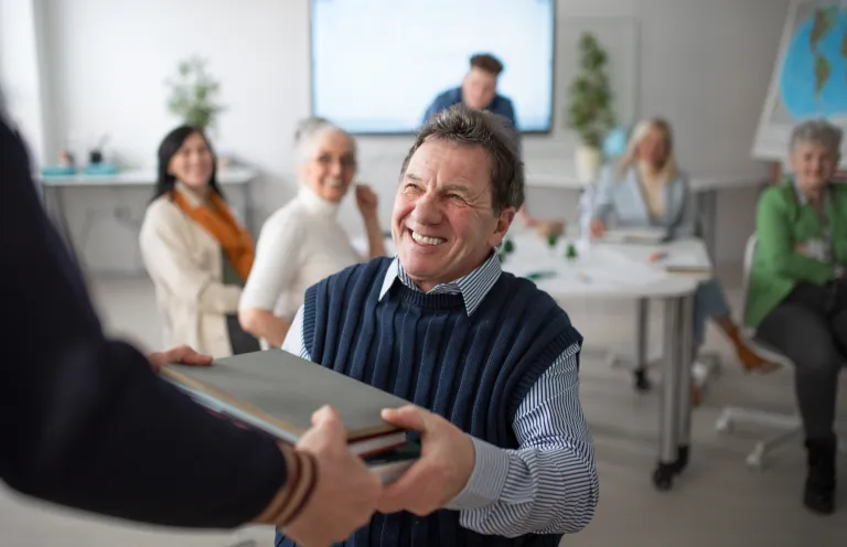 Doktoraty i habilitacje w UDDSW i FN WSB-DSW Merito | Uniwersytet Dolnośląski DSW we Wrocławiu: Senior siedzący na krześle, trzymający laptopa.