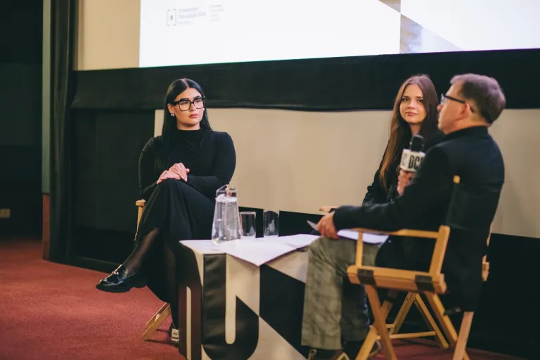 Studencki Dyskusyjny Klub Filmowy UDDSW zaprasza na kolejny film | 03.03.2026 | Aktualności | Uniwersytet Dolnośląski DSW we Wrocławiu: Dwie kobiety oraz mężczyzna siedzą przy stoliku i przeprowadzają wywiad.